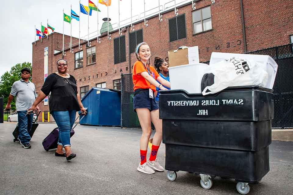 Student helping new 博彩网址大全 family move in, pushing cart to residence hall